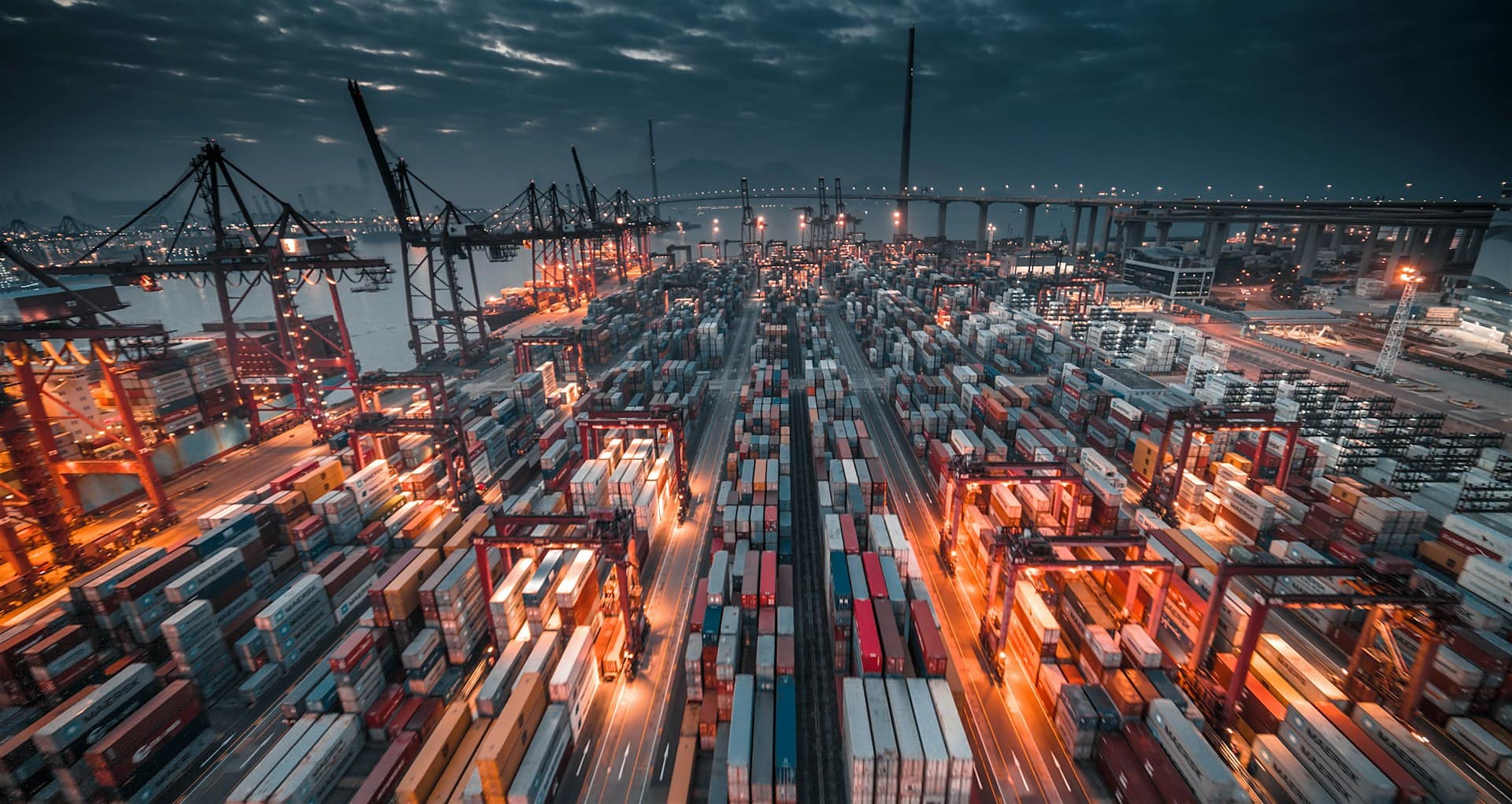 Stacked containers and cranes under a dark sky