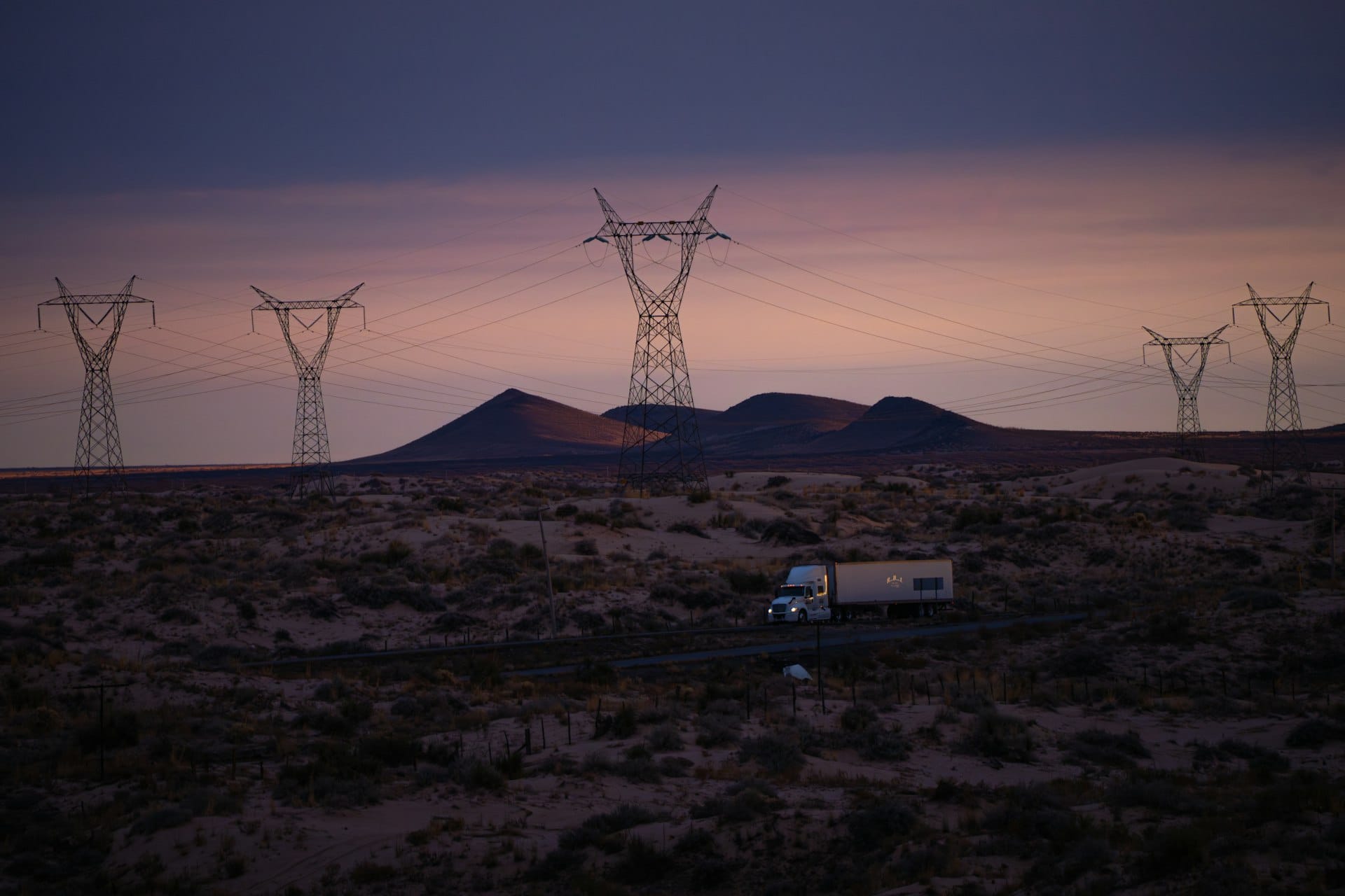 A truck on a desert road at dusk under power lines