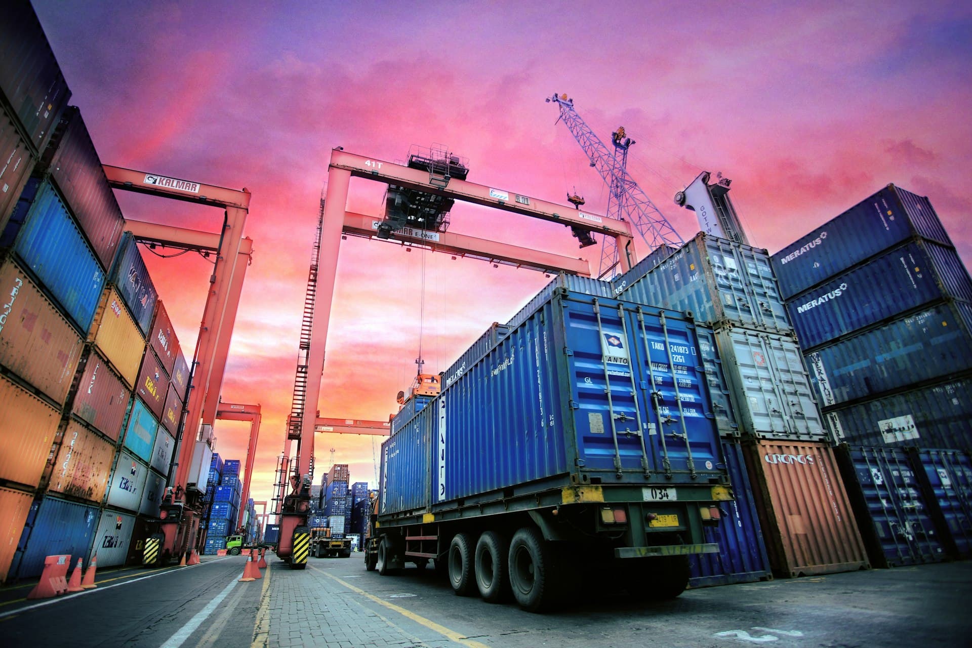 Truck passing between stacked shipping containers at dusk
